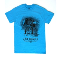 Frontside of a crewcut sapphire blue t-shirt with a grayscale illustration of a cameraman behind a large-format camera. Underneath is the H.H. Bennett Studio logo