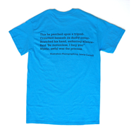 Backside of a crewcut sapphire blue t-shirt. Contains the text: 'This he perched upon a tripod-; Crouched beneath its dusky cover-; Stretch his hand, enforcing silence-; Said "Be motionless, I beg you!"; Mystic, awful was the process.' -Hiawatha's Photography, Lewis Carroll