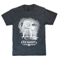 Frontside charcoal gray t-shirt with a grayscale illustration of a cameraman behind a large-format camera. Underneath is the H.H. Bennett Studio logo