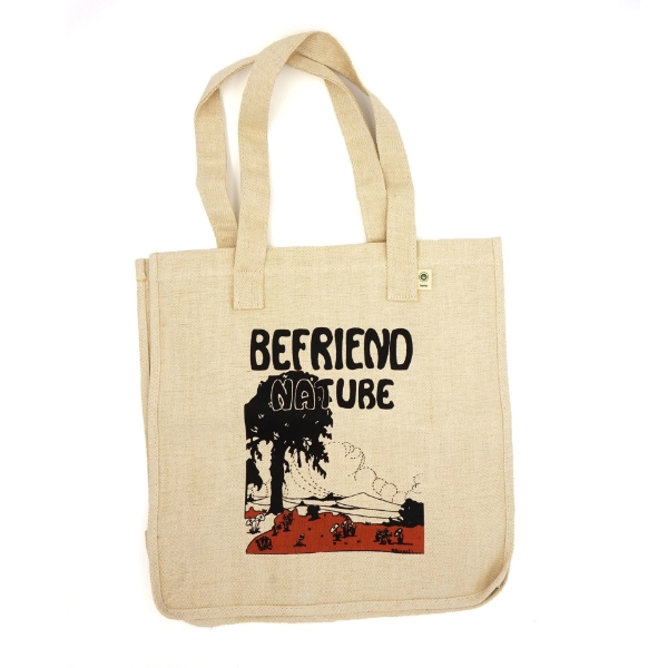 A tan colored tote bag with matching handles.  The illustrated image on the tote shows a big black tree, brown colored grass with white and black mushrooms, outlines of mountains in the skyline, and dotted lines indicating clouds. The text is in black vintage bubble letters and reads "Befriend Nature".