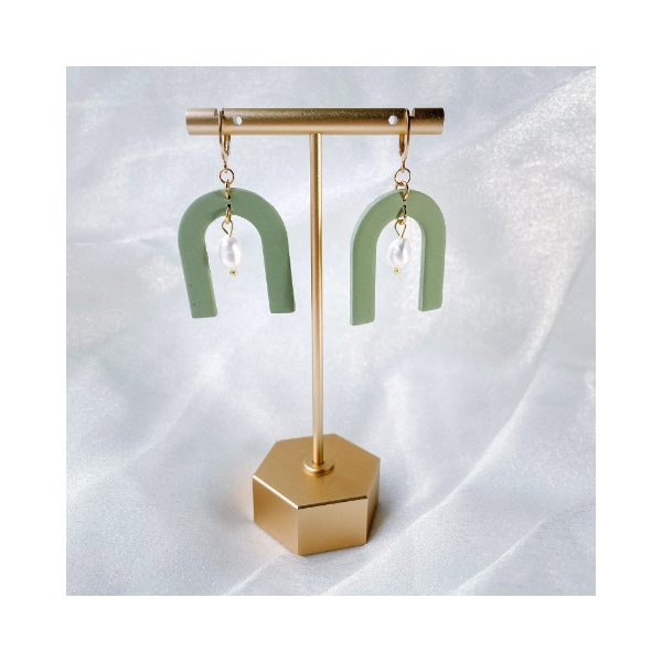 Two olive green dangle earrings in the shape of arches with a white river pearl positioned in the middle void of the arch.