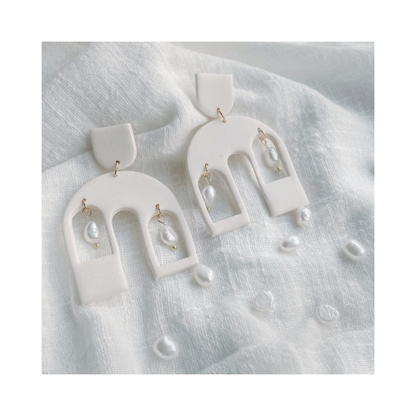 Two white dangle earrings with an arch shape design. Each arch has 2 rectangular cutouts with one faux river pearl suspended in each rectangle cutout.. 