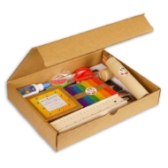 Brown cardboard box with lid open to expose contents, which includes craft supplies for kids, including colored pencils, crayons, a ruler, an art pad, popsicle sticks, and scissors.