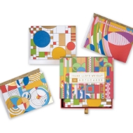 Colorful box surrounded by greeting cards with geometric designs by Frank Lloyd Wright. Pull-out drawer with ribbon tab.