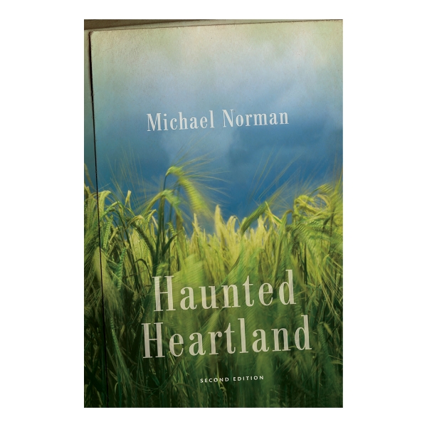 Book cover of "Haunted Heartland" by Michael Norman with picture of green corn stalks in a field under a cloudy sky. 