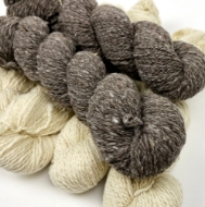 Close-up photo of several skeins of yarn, 4 natural white on bottom and 2 natural gray on top. 