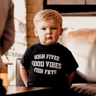 Toddler wearing black toddler size T-shirt that says "High Fives. Good Vibes. Fish Frys." The lettering is bold white.