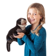Young blonde girl holding fuzzy brown river otter hand puppet with black webbed feet, fat tail, and little black ears. The girl wears a blue shirt and is smiling.  