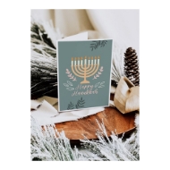Happy Hanukkah Menora Card sitting on a corner table with pine cone and frosted pine needles rested among sides. 