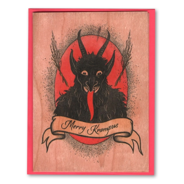 Krampus Wood Card front featuring a Krampus smiling with red tongue out in front of a red background and a banner reading "Merry Krampus." Wood grain card with a red envelope. 