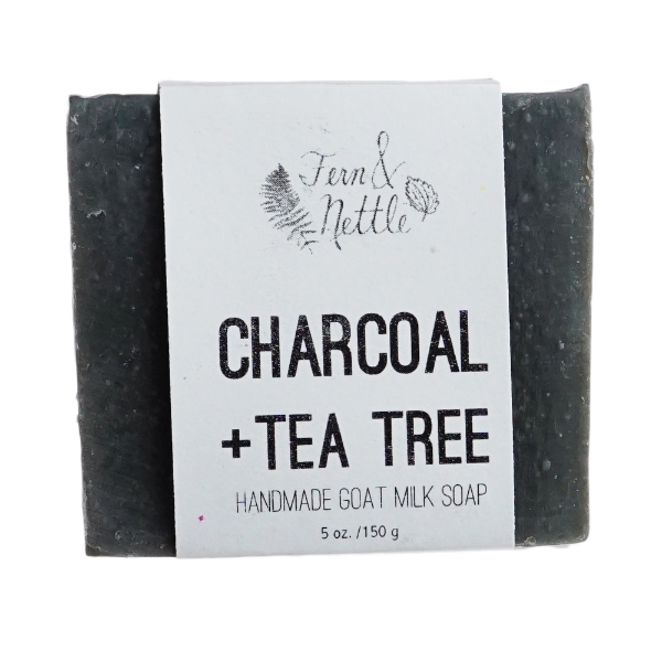 Square bar of dark gray soap with white paper label wrapped around it. The label says "Charcoal + Tea Tree."
