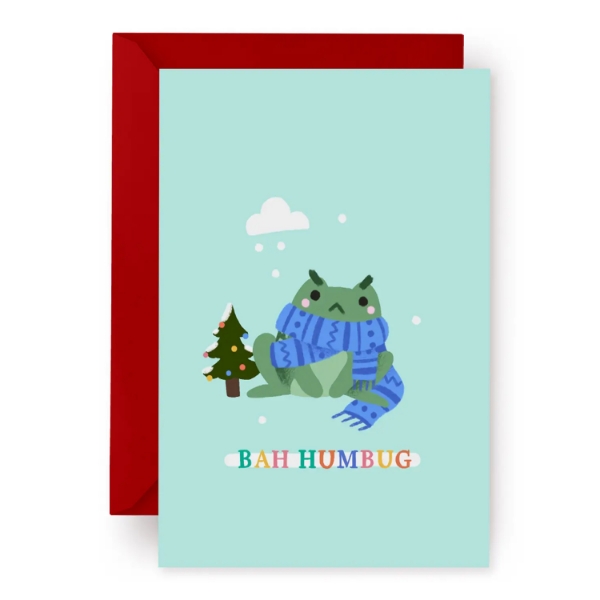 Greeting card with illustration of a green frog wearing a scarf. Light green background and the words "Bah Humbug" below the frog in multicolor bold font.