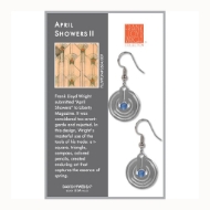 Two short, polished metal, dangle earrings with perforated round shape and blue glass bead in center. Shown on informational display card.
