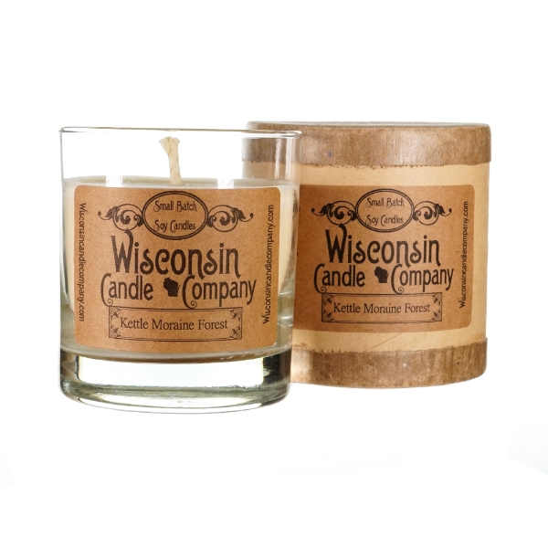 Kettle Moraine Forest candle in clear glass sitting next to brown wood container. The white wax with white wick candle has brown labeling with black text. 