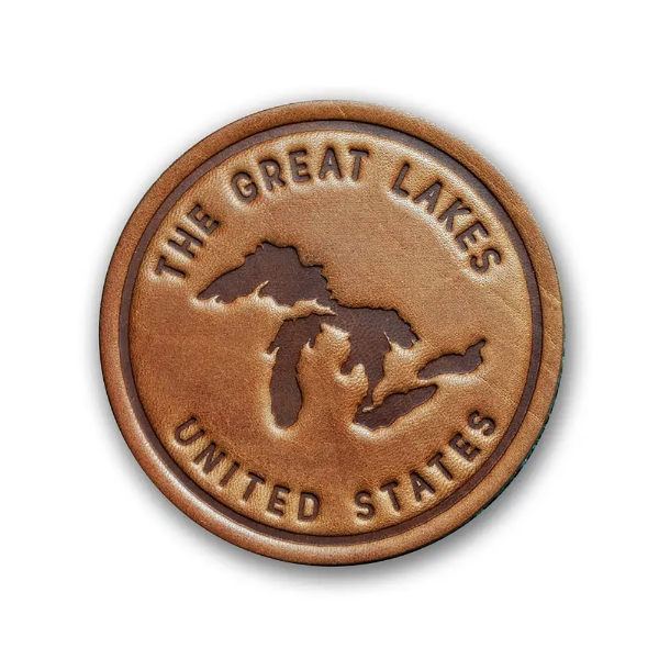 Round leather coaster, brown, with embossed, bold font that says "Great Lakes United States" and there are embossed shapes of the five lakes in dark brown. 