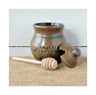 Brown, stoneware honey pot with cover and wooden honey dipper. Honey dipper and cover are left and right of the honey dipper, all resting on tan burlap.