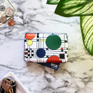 Rectangular clasp-closure wallet with Frank Lloyd Wright geometric design with colorful circles and black lines. Pictured on countertop next to money and keys to show size.