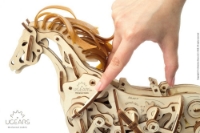 Close-up of mechanical wooden horse model by Ugears shown from side, facing left, made from small, laser-cut pieces of thin plywood. A hand points at a part on the horse's shoulder.