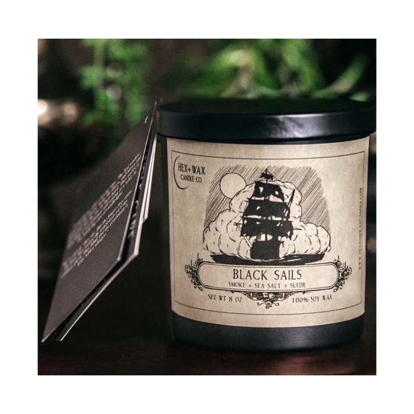 "Black Sails" candle from Hex + Wax Candle Company. Dark glass container, black metal lid, tan paper label with illustration of sailing ship in black ink.