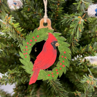Holiday tree ornament carved from gourd and featuring red cardinal perched in round, green wreath. 