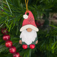 Holiday tree ornament representing a gnome figure. Carved from gourd and hand painted red hat, white beard, and red shoes. 