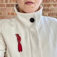 Red brooch in shape of cardinal. Hand carved from natural gourd. Shown pinned on light tan jacket.
