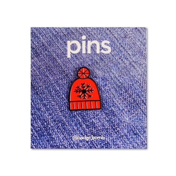 An enamel pin of a red winter hat with a snowflake design.