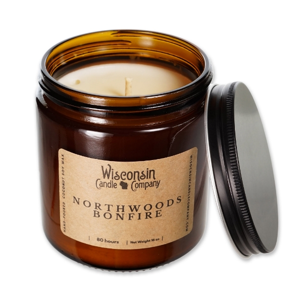 The Northwoods Bonfire 16 oz candle in brown glass container, open, with black metal screw-on lid leaning on side of jar.