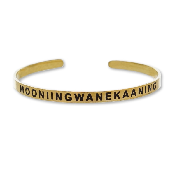 Brass tone Madeline Island Museum souvenir cuff bracelet with the word "Mooniingwanekaaning" stamped in black.