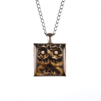 Square pendant with geometric lotus flower design in dark brown tones. 